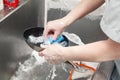 Closeup of dishwasher in uniform washes a pan with foam and a sponge under the tap water in a metal sink in the restaurantÃ¢â¬â¢s Royalty Free Stock Photo